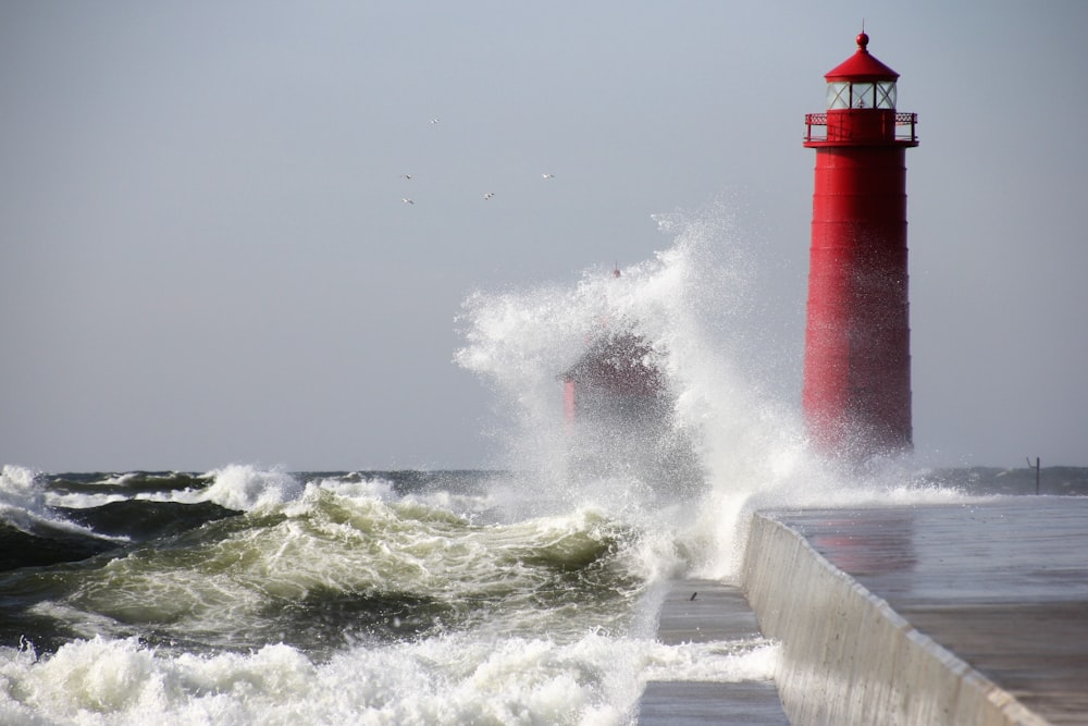 waves crushing the red lighthouse under gray sky during daytime