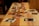 Several printed photographs are scattered across a wooden table. The photographs vary in orientation and depict different scenes or subjects, creating a nostalgic and artistic arrangement. The warm tones of the wood complement the varied colors in the photographs.