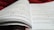 An open book with pages filled with mathematical formulas and text. The writing includes complex equations and mathematical symbols spread across two facing pages. The background is soft and out of focus, with what appears to be a red fabric.
