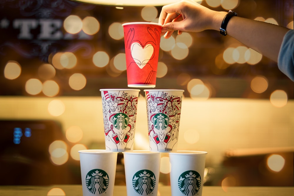 person stacking five assorted-color Starbucks cups