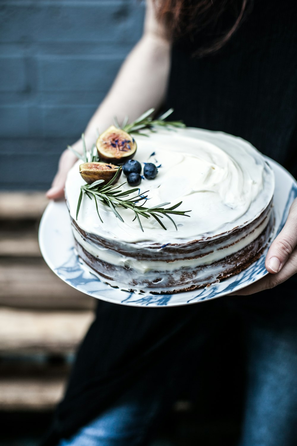 person holding round white icing-covered cake with blue berry on top