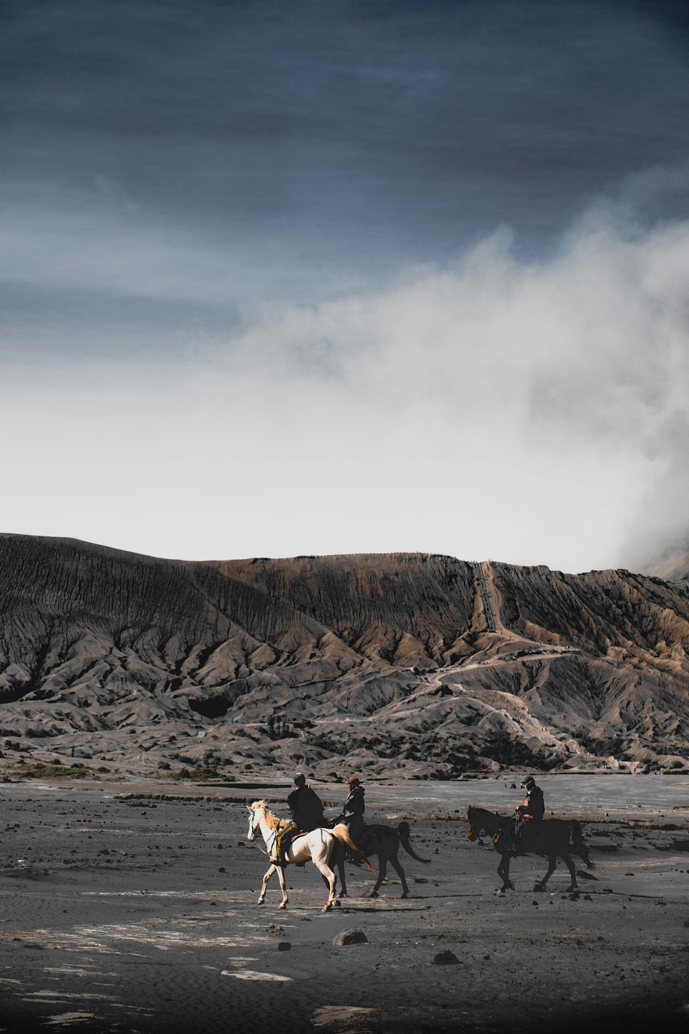 three person riding on horse near mountain under white clouds