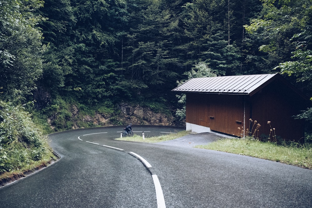 Casa de madera marrón al lado de la carretera asfaltada rodeada de árboles durante el día