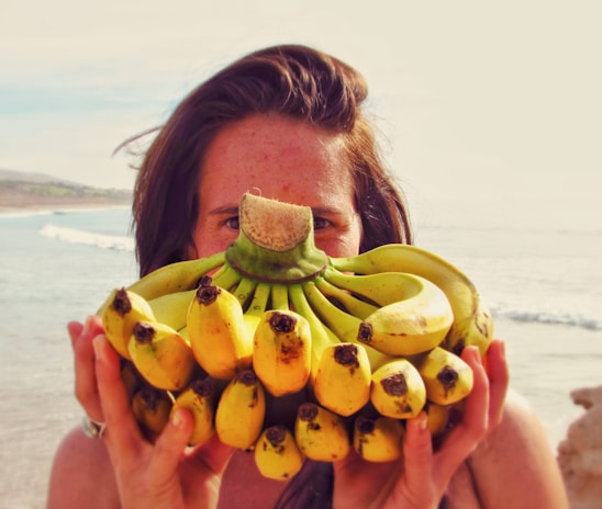 Smiling farmer holding a bunch of freshly harvested green bananas in a vibrant field.