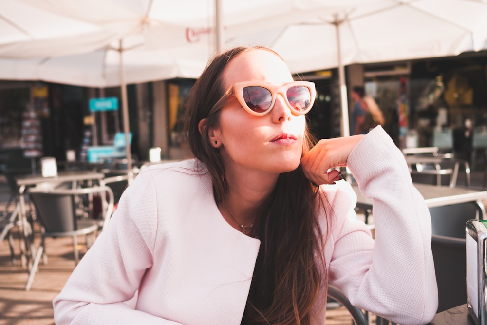 woman in orange framed sunglasses sitting under white umbrella