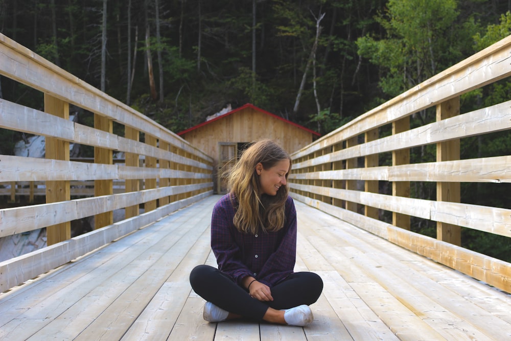 Donna che si siede sul ponte di legno vicino alla foresta