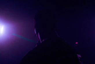 A moody still from a dark-themed music video featuring a silhouette against neon lights.