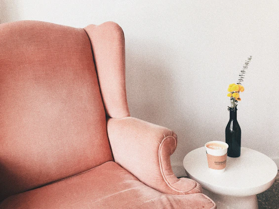 A cozy scene with a pastel pink ceramic mug resting on a wooden table beside a small vase of fresh flowers.