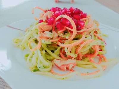 A plate of colorful spiralized vegetables topped with bright red pomegranate seeds, creating a fresh and vibrant presentation.