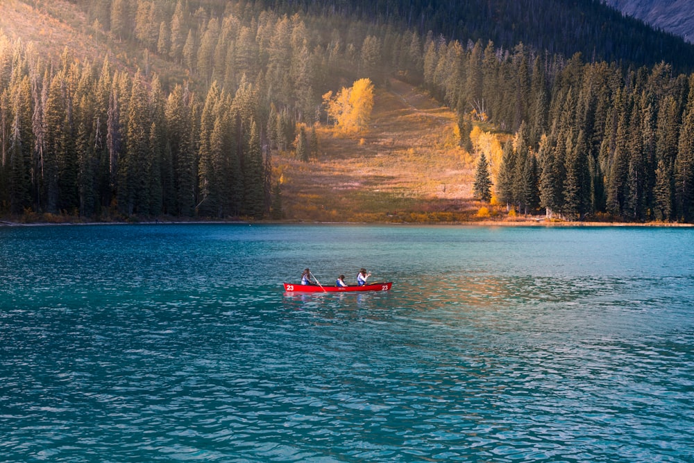 three person in red rowboat on blue calm body of water at daytime