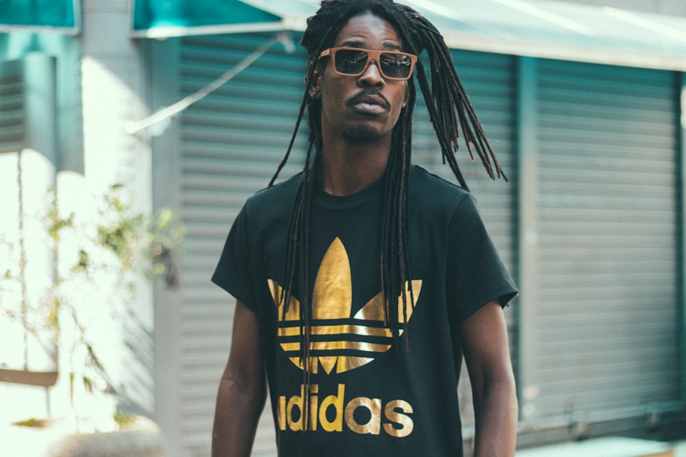 man with dreadlocks hair wearing black and gold Adidas crew-neck shirt