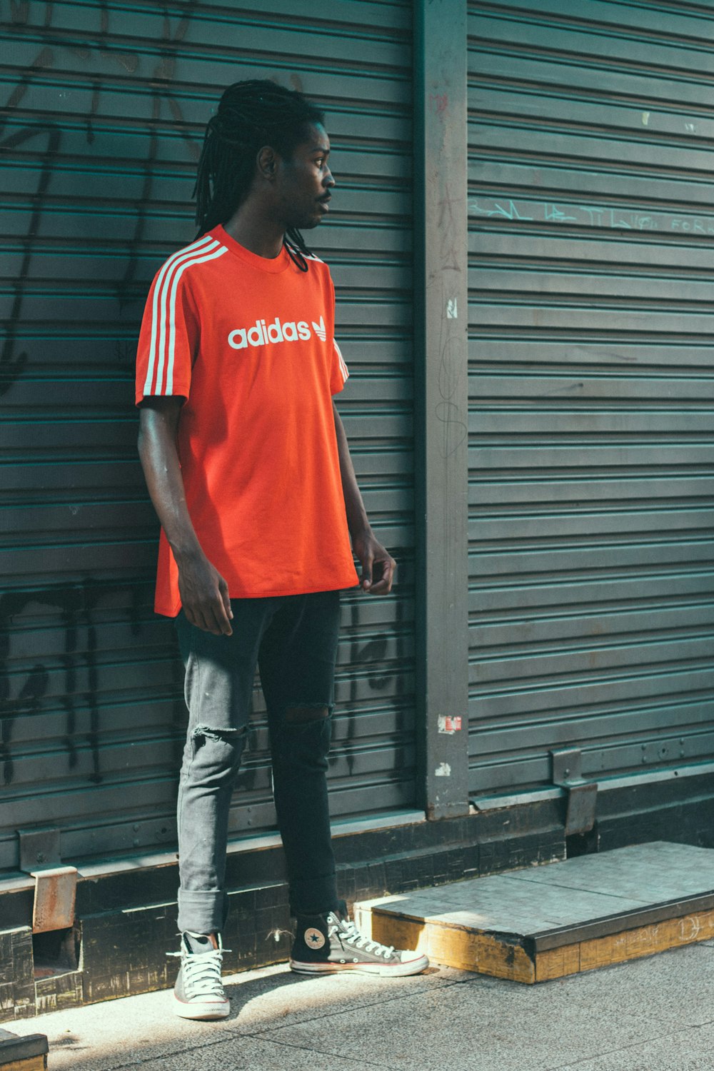 man wearing red Adidas t-shirt in front of roller shutter