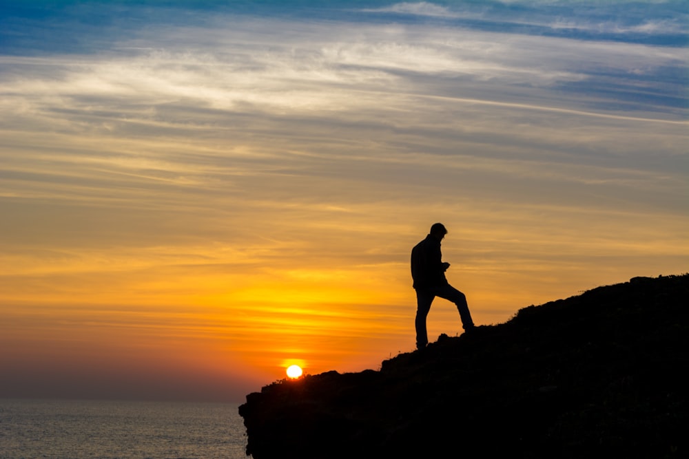 sihouette of person standing on rock formation during golden hour