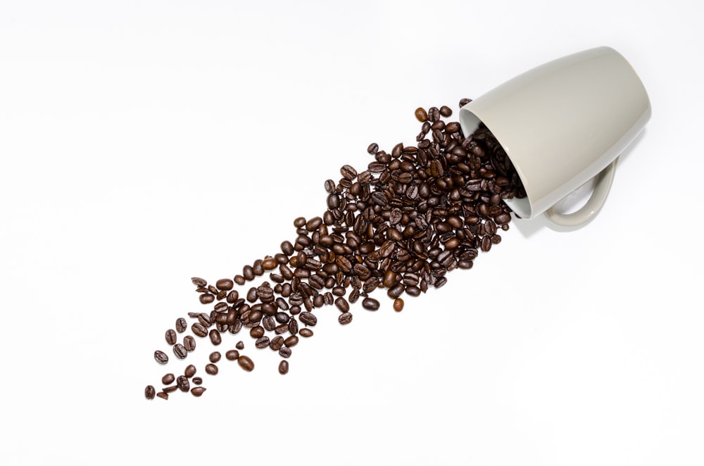granos de café junto a una taza de cerámica gris
