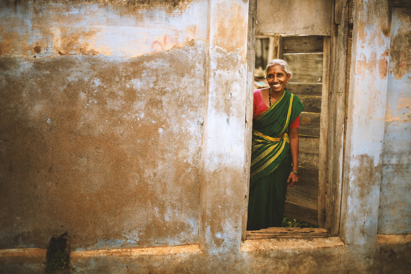 A smiling woman in a sari standing near a doorway