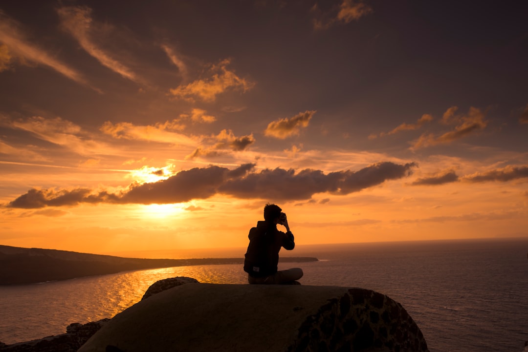 silhouette of person sitting on hill near body of water