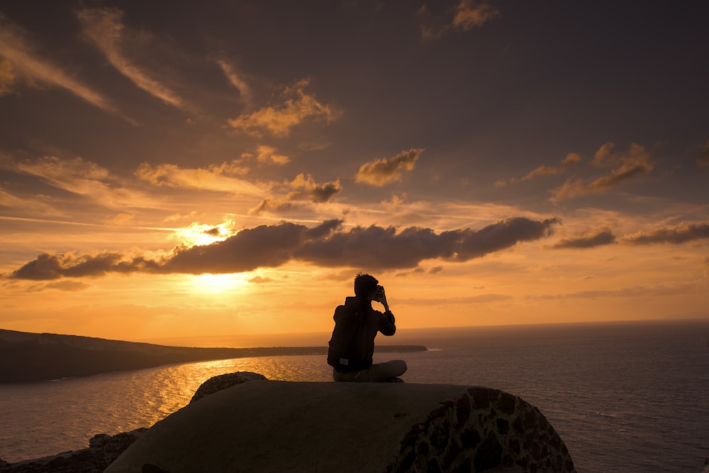 silhouette of person sitting on hill near body of water