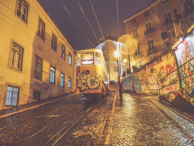 The graffiti-covered Elevador da Gloria funicular climbing a steep lit street toward Bairro Alto at night