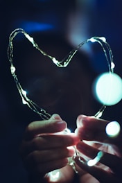 Hands holding a glowing heart-shaped light in a dark room