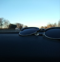 Close-up of a car key and sunglasses resting on a dashboard with a beach scene outside.