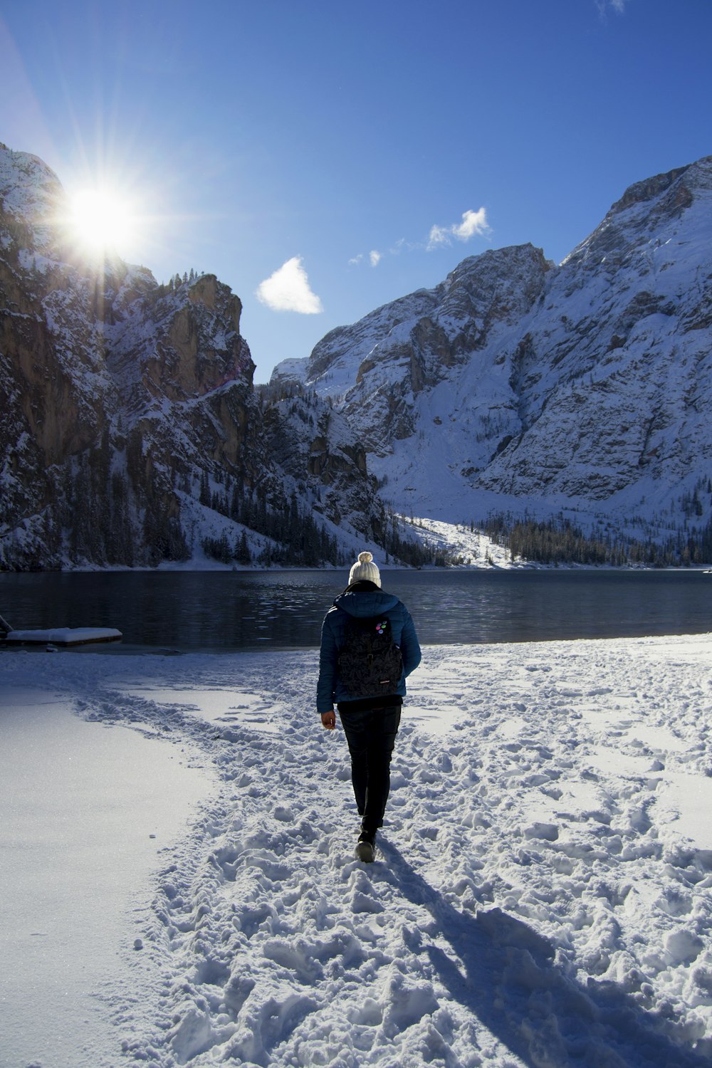 person walking on snow near body of water and mountains