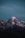 A snow-capped mountain peak set against a dark blue sky, with the soft glow of twilight accentuating the rugged textures and features of the rocky summit.