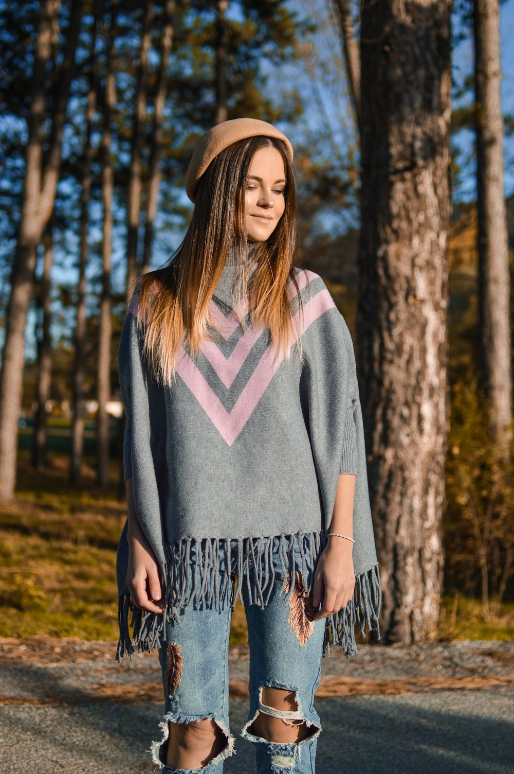 woman standing while looking down and smirking near trees at daytime