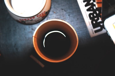 Close-up of a steaming cup of dark roast coffee on a desk cluttered with transit maps.