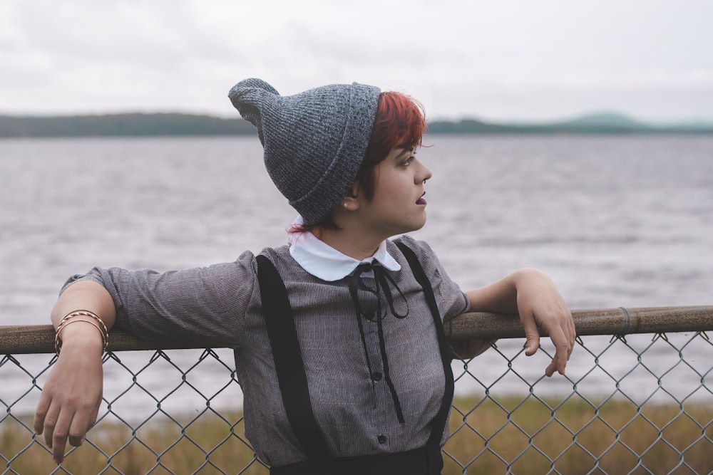 woman leaning on chain link fence near body of water