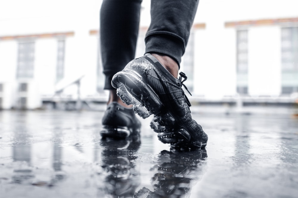 person wearing black Nike Vapormax shoes on wet floor