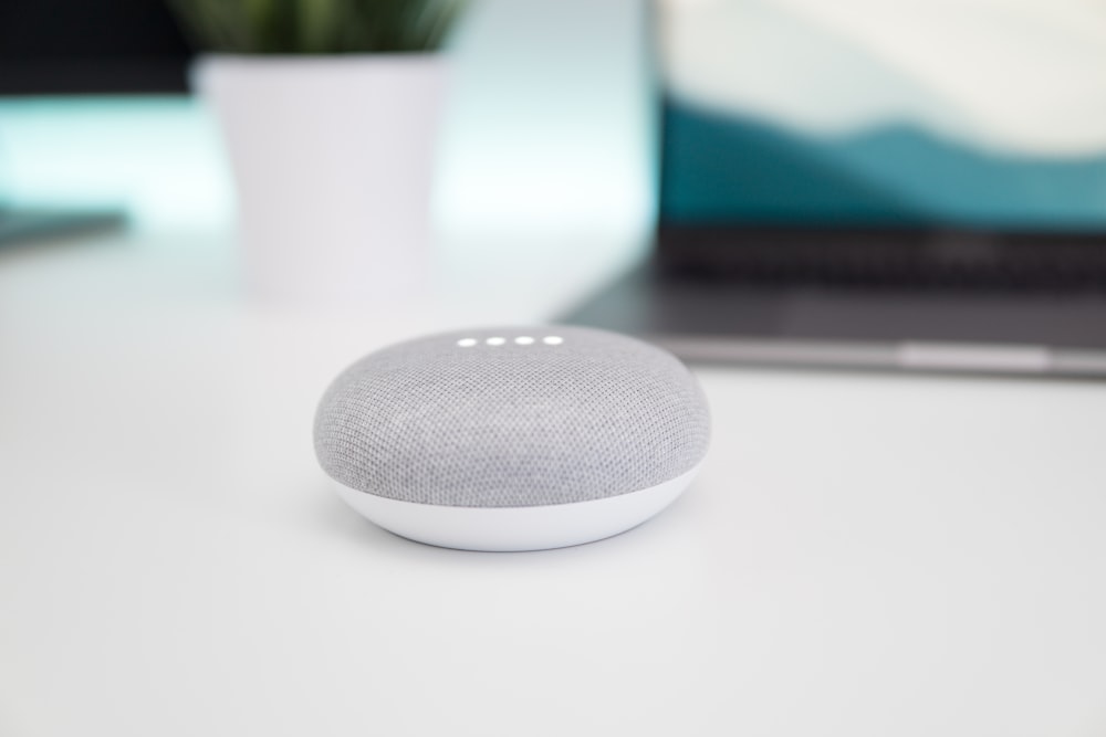 acceso l'altoparlante Google Home Mini grigio e bianco su superficie bianca