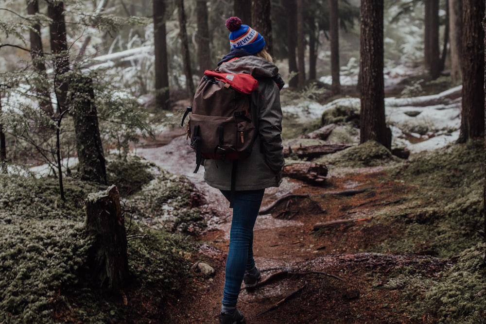 woman with brown backpack walking near the trees