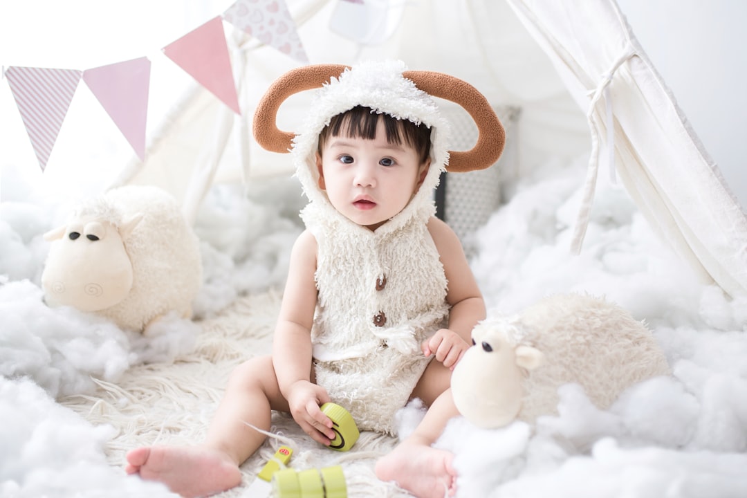 baby sitting beside white sheep plush toy