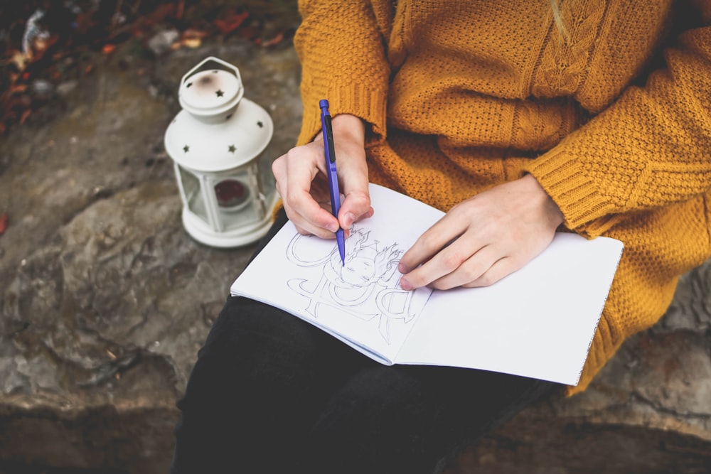 Persona che disegna sul quaderno da disegno vicino alla lanterna bianca
