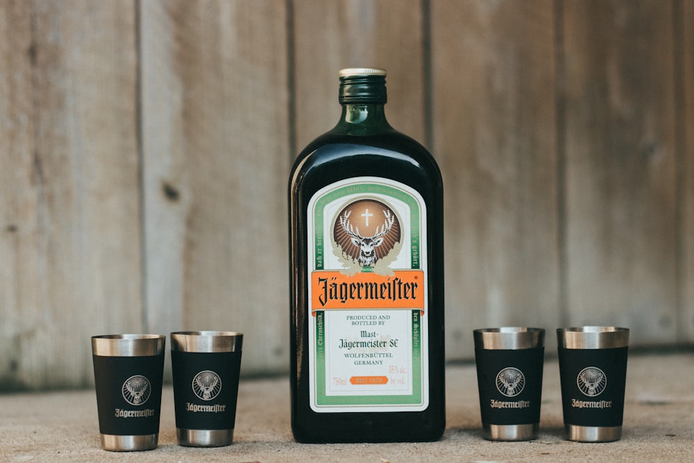 green and white glass bottle beside four stainless steel drinking cups