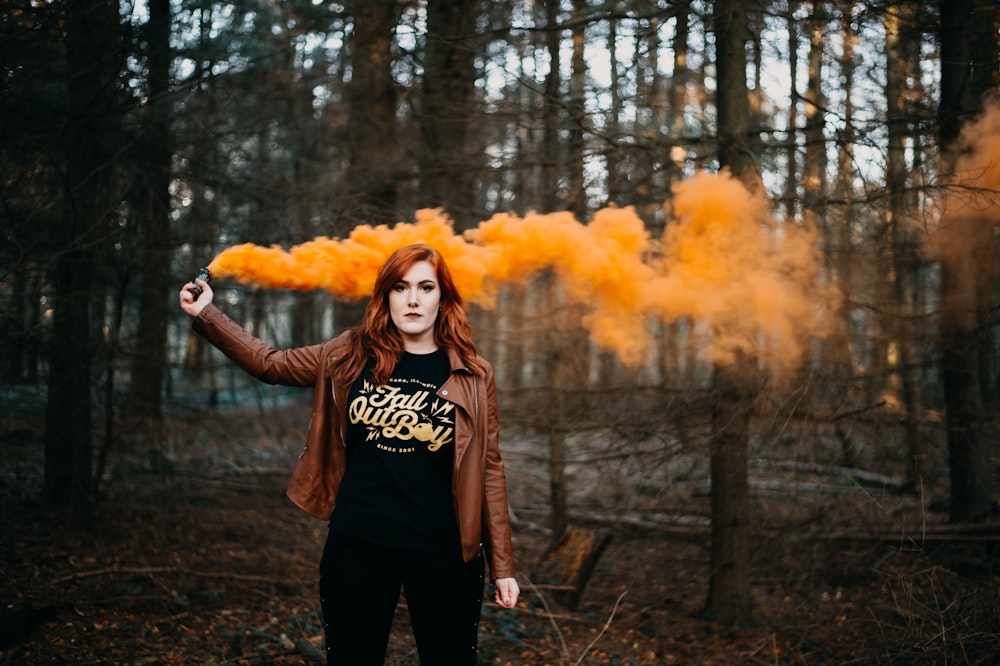 woman holding on her hand orange smoke flare near tree