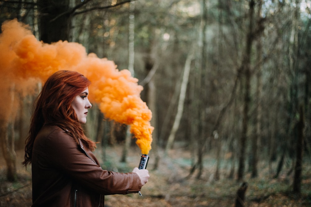 Donna che tiene polvere di fumo arancione circondata da alberi durante il giorno