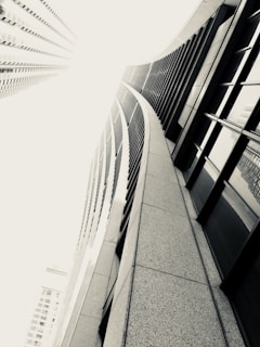 A dramatic view of tall skyscrapers emphasized by a unique angle, with the perspective drawing the eye upward along the curved lines of the building. The monochromatic color scheme adds a sense of modernity and sophistication.
