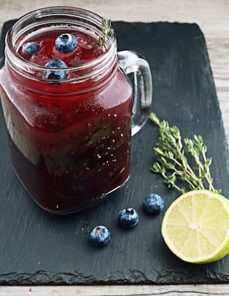 clear glass mason jar with red liquid and lemon beside