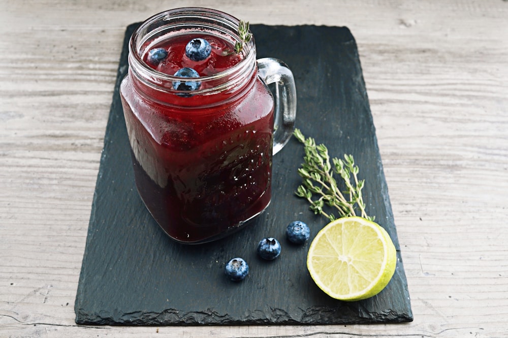 clear glass mason jar with red liquid and lemon beside