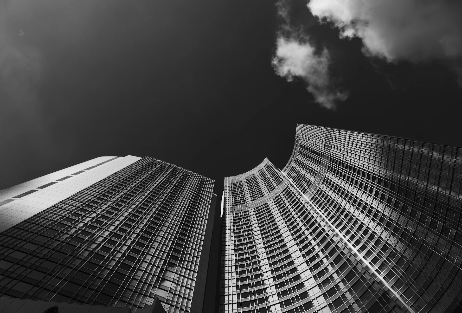 A dramatic black-and-white shot of towering city skyscrapers disappearing into low-hanging clouds.