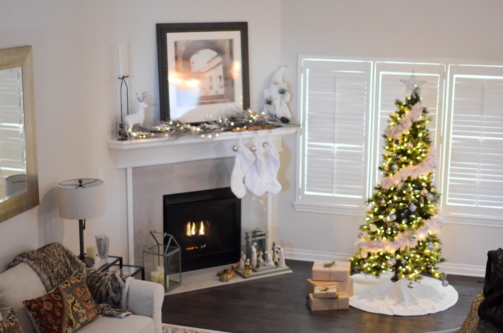 Christmas tree with string lights turned on near electric fireplace inside room