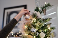 person putting bauble on top of Christmas tree