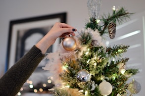 person putting bauble on top of Christmas tree