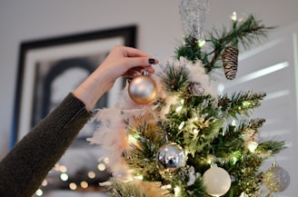person putting bauble on top of Christmas tree