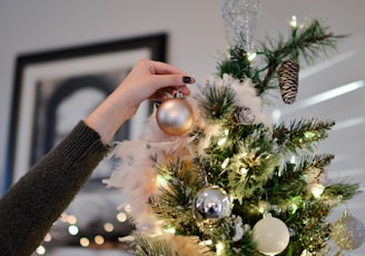 person putting bauble on top of Christmas tree