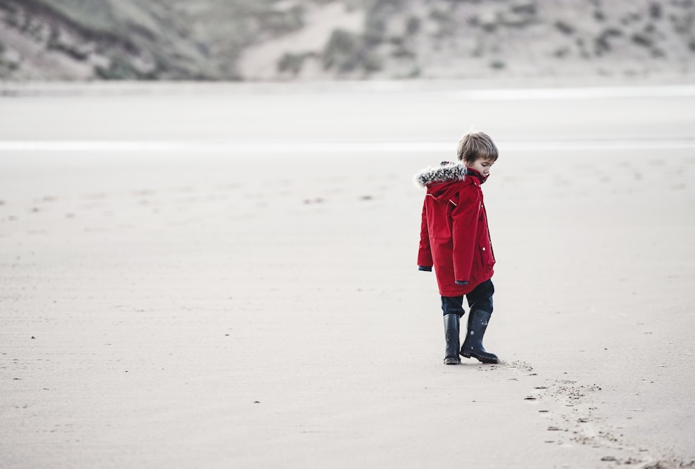 boy walking on sand with tracks