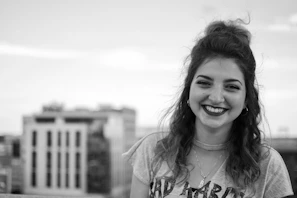 Woman wearing a layered crystal necklace, smiling softly with a serene cityscape behind her