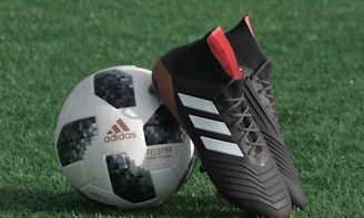black adidas cleats lean on white and black adidas soccer ball on green grass