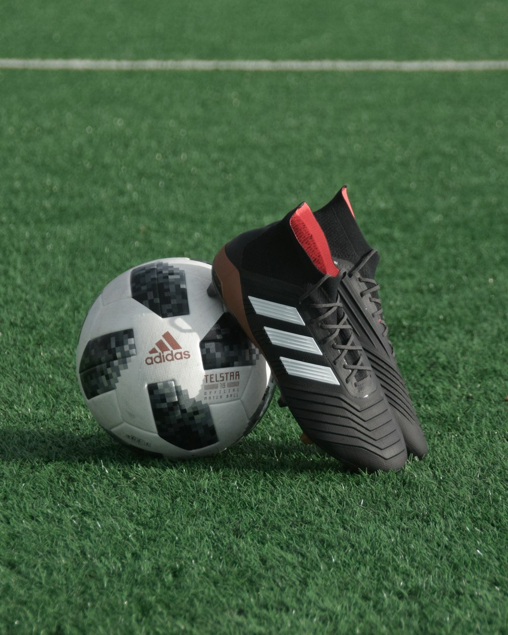 Schwarze adidas Stollen auf weißem und schwarzer adidas Fußball auf grünem Rasen